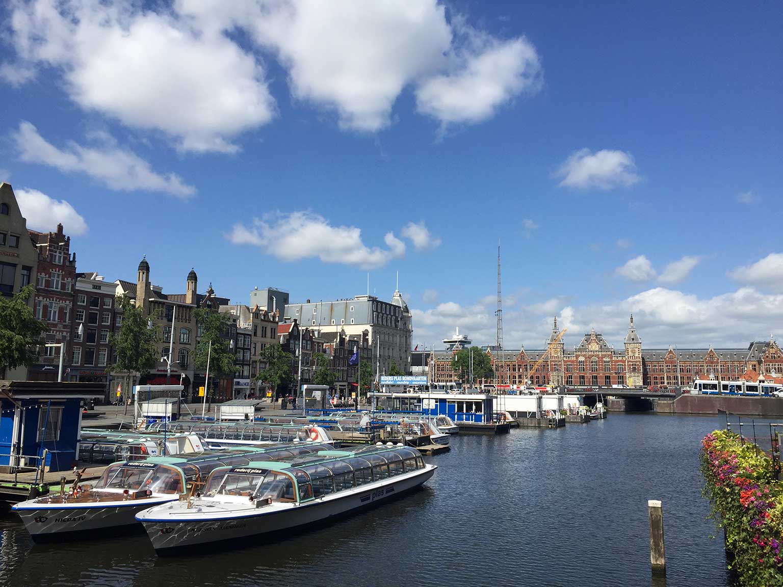Tour boats in the water of Damrak, Amsterdam, seen from Oudebrugsteeg towards Central Station
