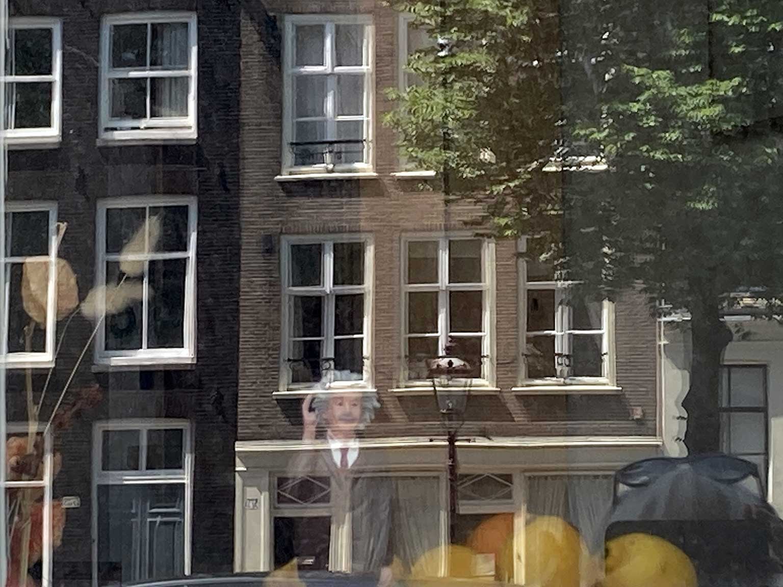 Pop van Albert Einstein achter raam op Prinsengracht, Amsterdam, met reflectie van huizen