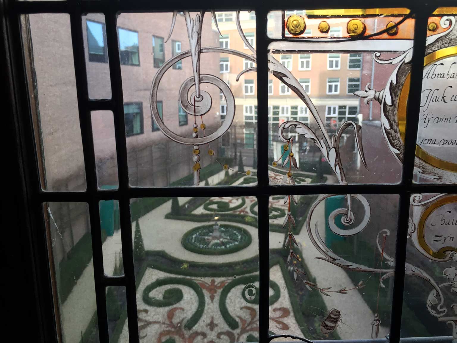 Zicht op de tuin van het Museum Willet-Holthuysen door een glas-in-lood raam